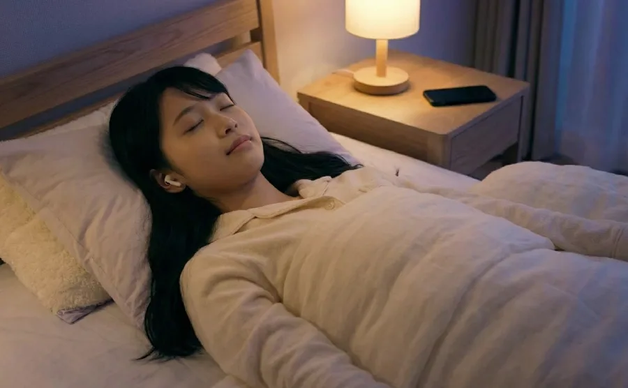 スマホを遠ざけて寝つこうとしている女性の画像