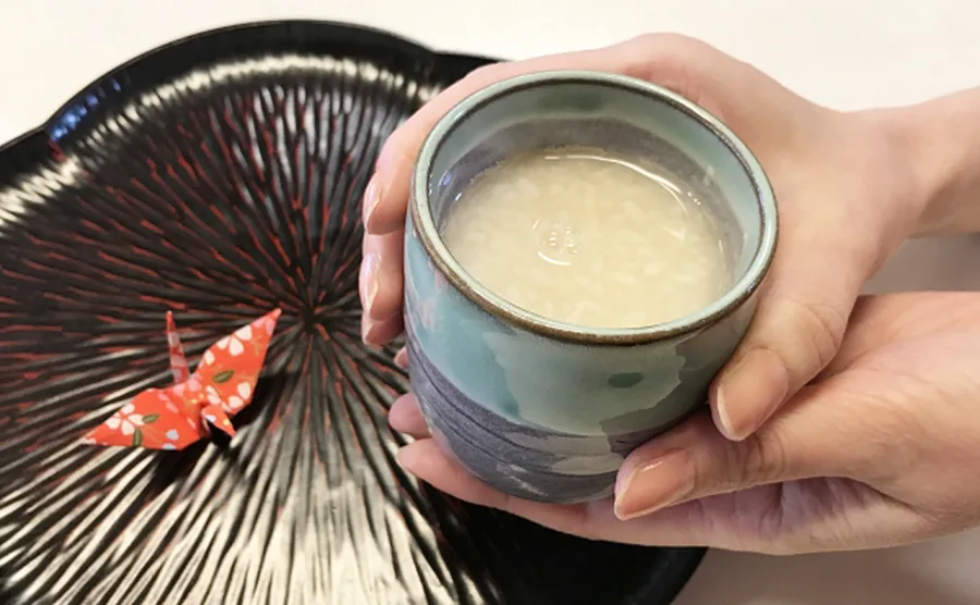 美味しそうな甘酒の入ったカップを手で持っている画像