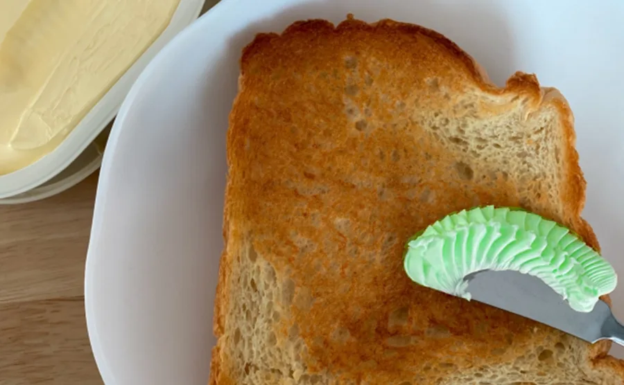 モリンガを混ぜた緑のマーガリンをパンに塗るところの画像