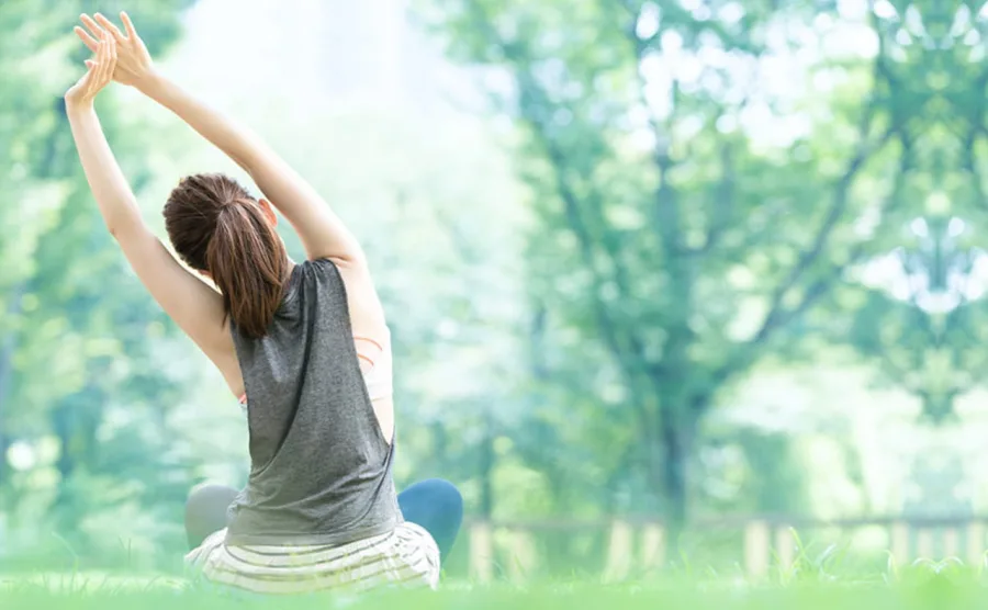自然の中に座って両腕を伸ばしてストレッチしている健康的な女性の後ろ姿の画像