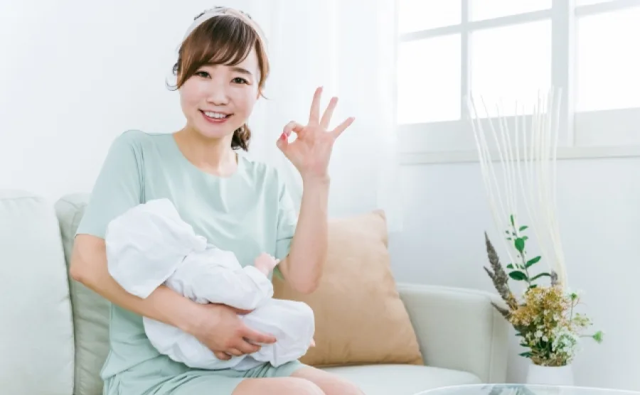 赤ちゃんを抱えてOKポーズをしている女性の画像