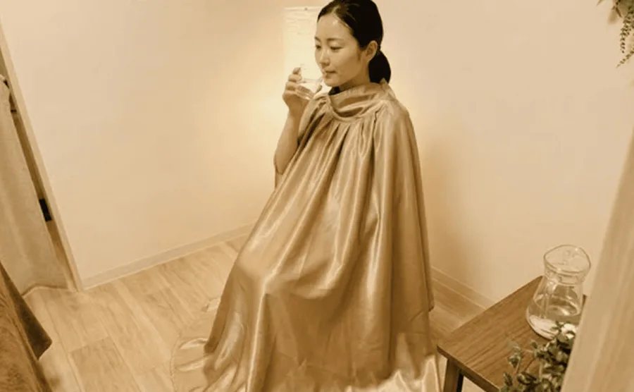 モリンガ蒸しを体験中の女性。専用マントに包まれた施術風景とよもぎ蒸しとの違いを比較