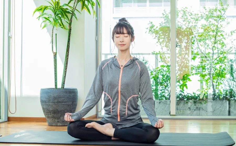 自室でヨガのポーズをして瞑想している女性の画像