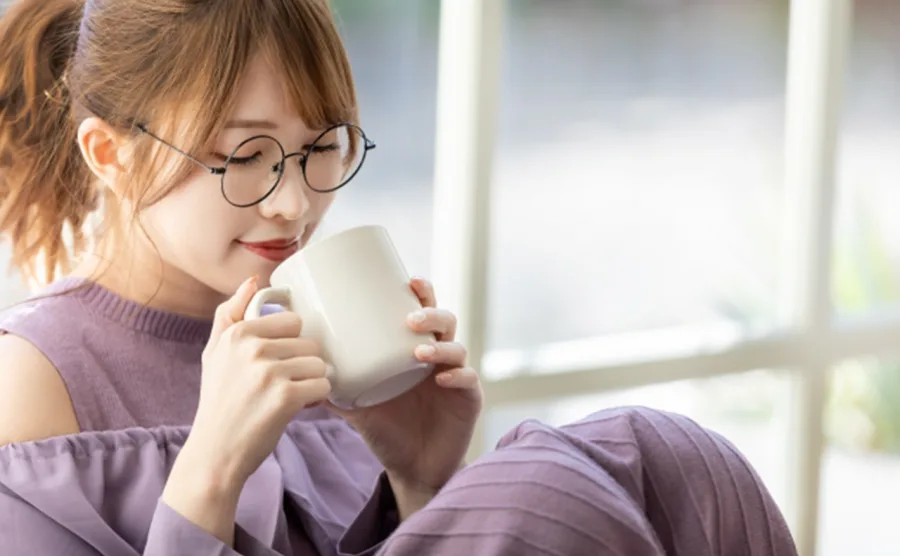ソファに寄りかかってあたたかい飲み物を飲んでいる女性の画像