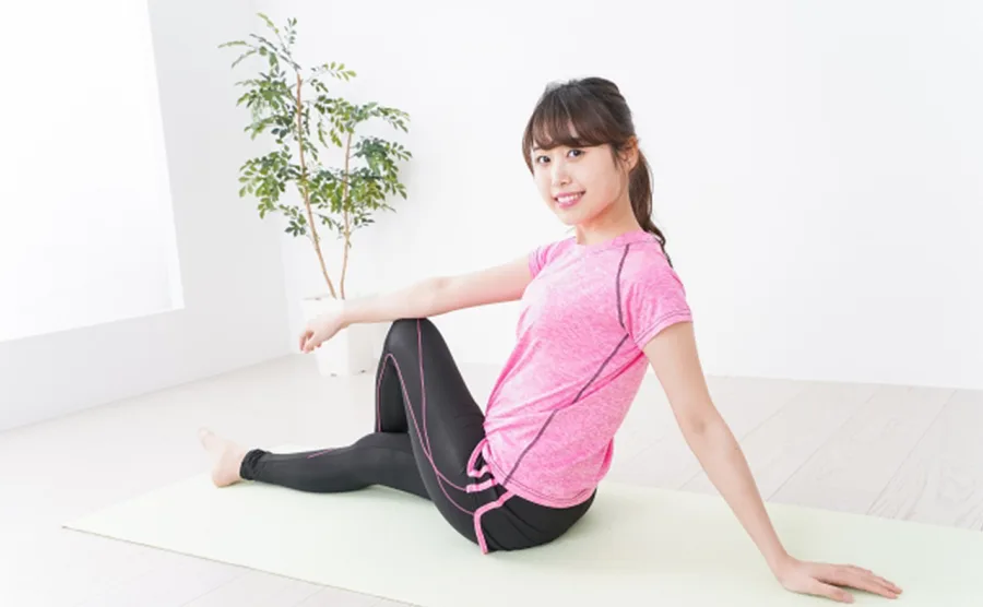 自室でストレッチをするピンクのトレーニングウェアを着た女性の画像