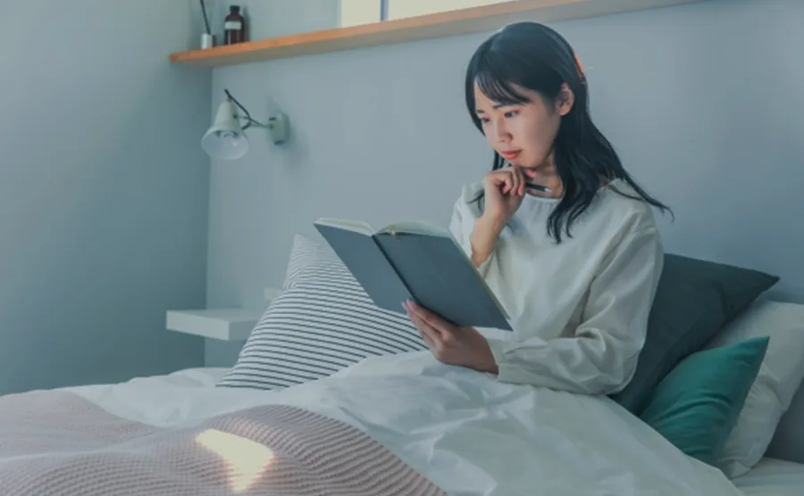 ベッドにもたれて日記を書いている女性の画像