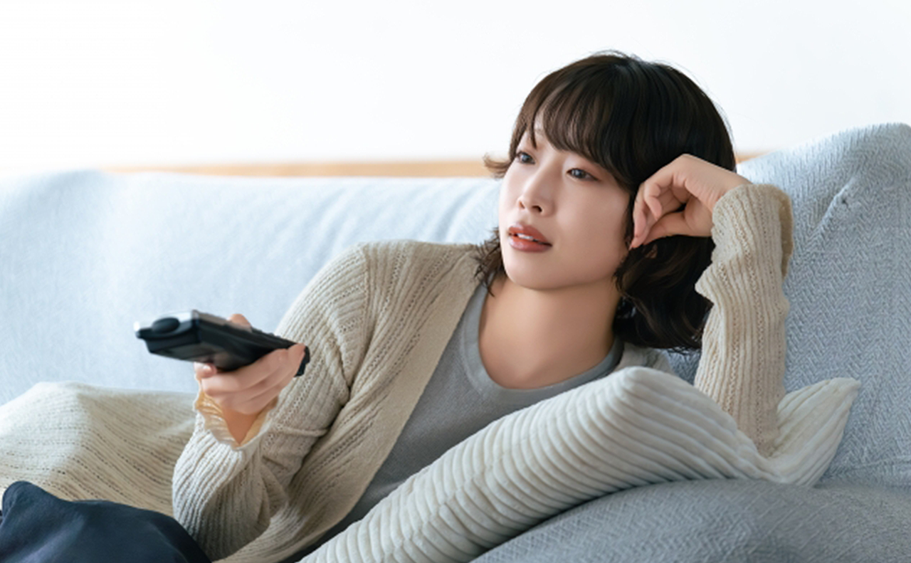 テレビのリモコンを持ってチャンネルを変えようとしている女性の画像