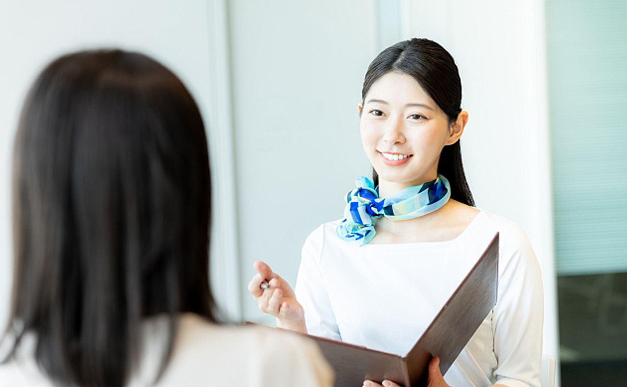 美容クリニックの受付で、若い女性がファイルを持って案内している画像